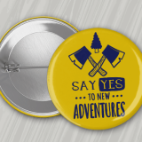 Yellow 1.25" round pin back button with navy blue imprint featuring crossed hatchets and the text 'Say Yes to New Adventures.