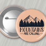 Peach colored 2.25" round button with pin back featuring the phrase 'Mountains are calling