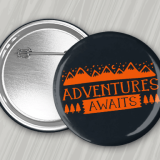 Black 3" round pin back button with orange 'Adventure Awaits' logo